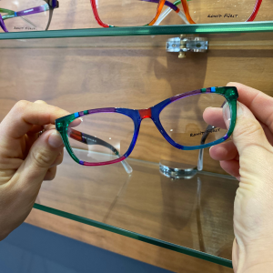 Two hands holding a pair of colourful glasses with the Ronit Furst logo on the lens.