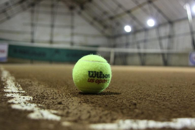 A tennis ball resting on the ground of a sports hall.