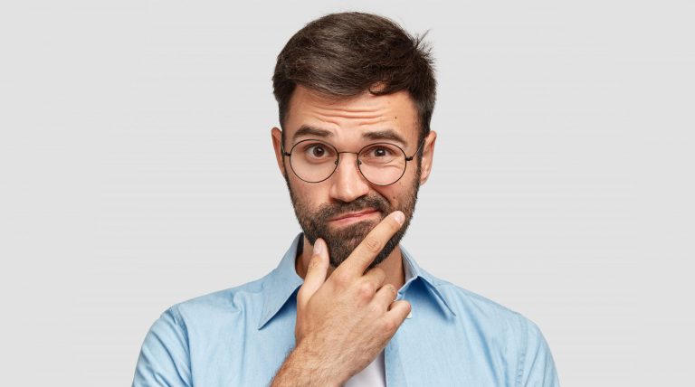 A young man wearing glasses looking confused.